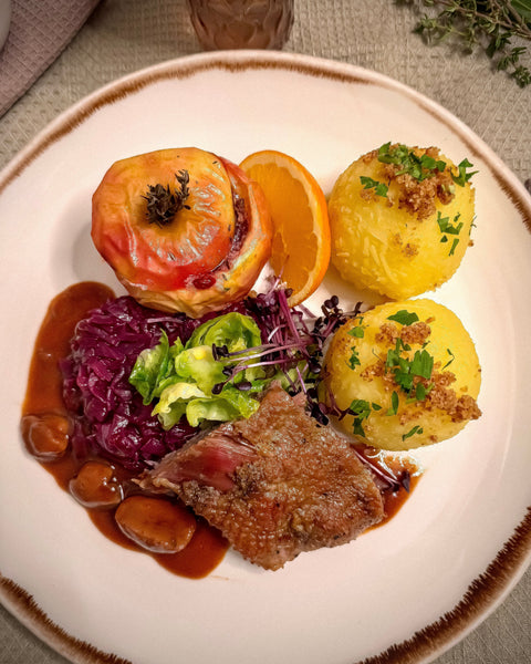 Gänsebraten mit Maronenjus, Rotkohl, geschwenkten Rosenkohl-Blättern, Kartoffelklößen und mit Preiselbeeren gefüllter Birne